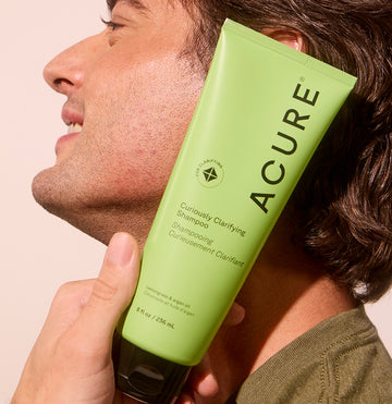 Man holding Curiously Clarifying Shampoo tube against his face, focusing on hair freshness